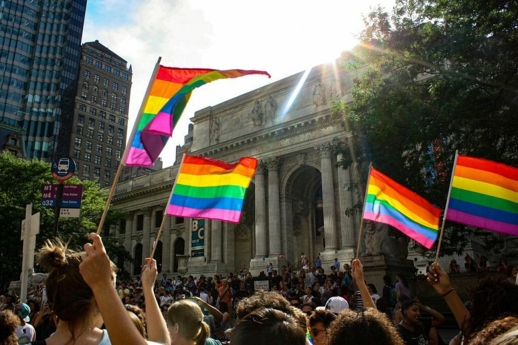 A crowd waves Pride flags in front of a government building.