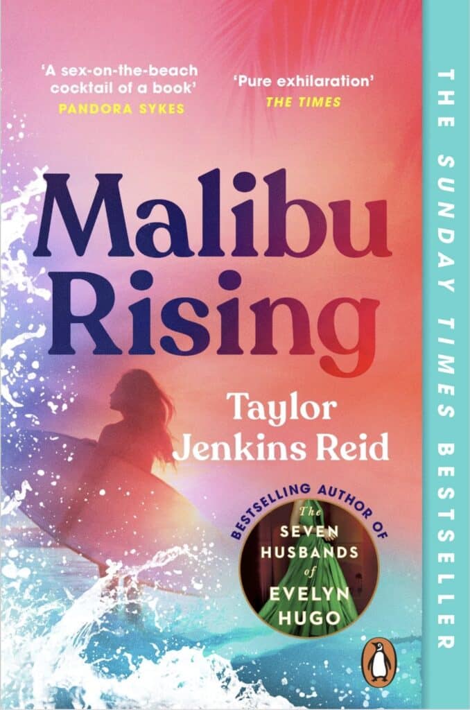 Image of book cover. cover is mixed gradient of pink and peach with sea foam and turquoise sea encroaching onto the cover at the bottom. In large indigo to red gradient writing are the words 'Malibu Rising' below this title is a silhouette of a woman carrying a surfboard and in white writing the author's name, Taylor Jenkins Reid. Below this in a small circle is an image of a woman in a green dress and the words Bestselling author of The Seven Husbands of Evelyn Hugo.
