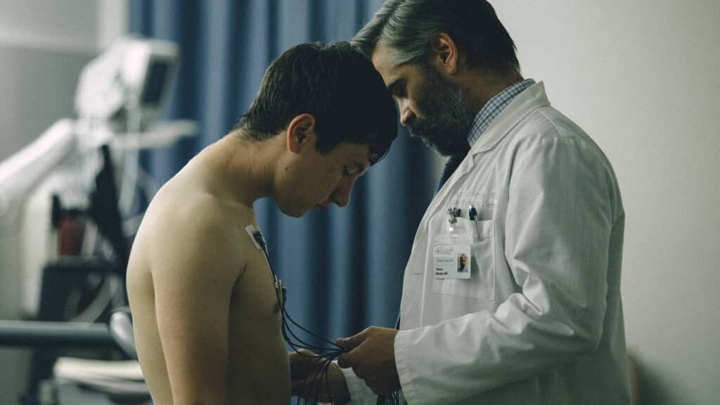 A doctor is treating a young man, they are in close contact with each other almost bowing their heads. The doctor is checking the young man's heart.