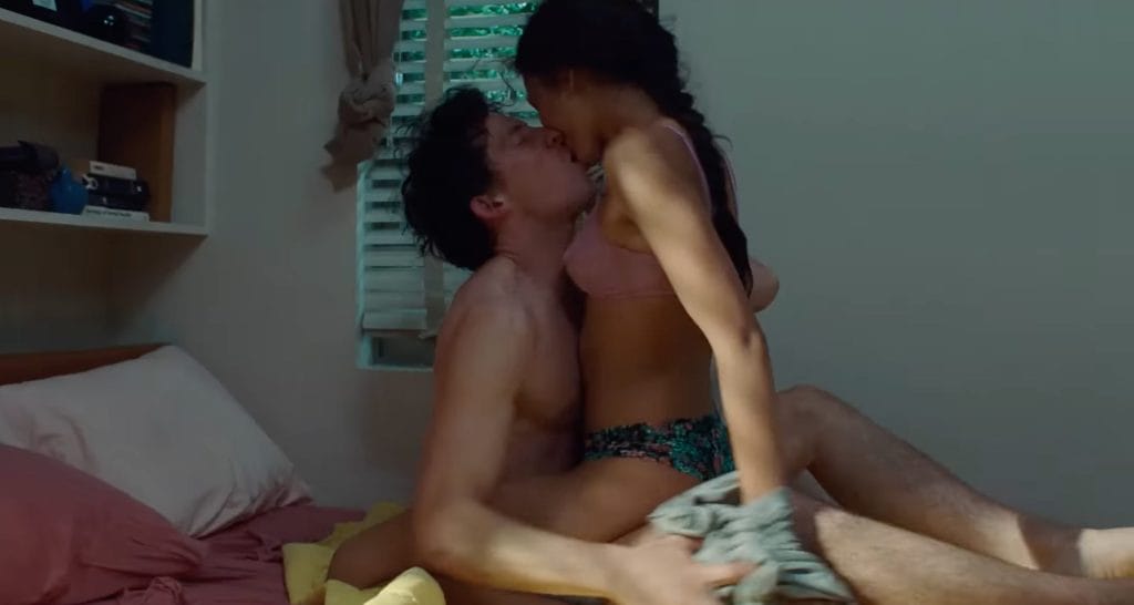 A man and woman, half-naked, kissing on a bed.