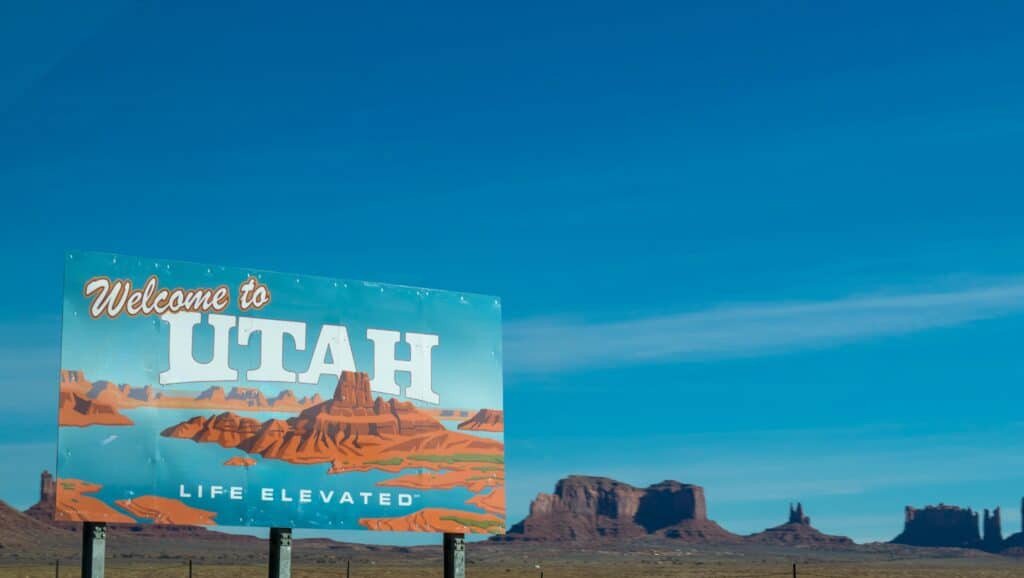 Utah sign with blue sky behind it and desert formations
