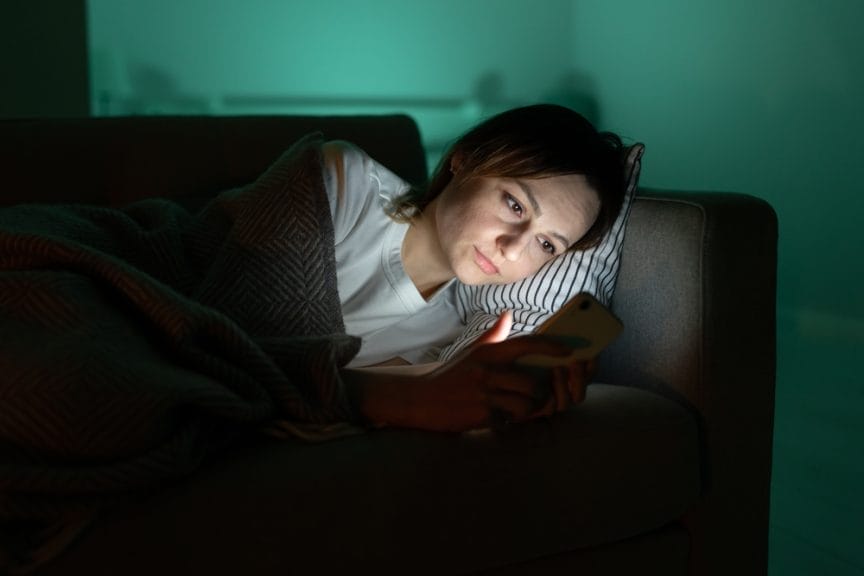 woman in bed looking on her phone screen time blue light sleep routine sleep hygiene sleep quality