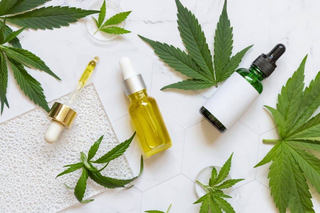 CBD oil bottles are laid against a white background. Cannabis leaves are scattered around them.