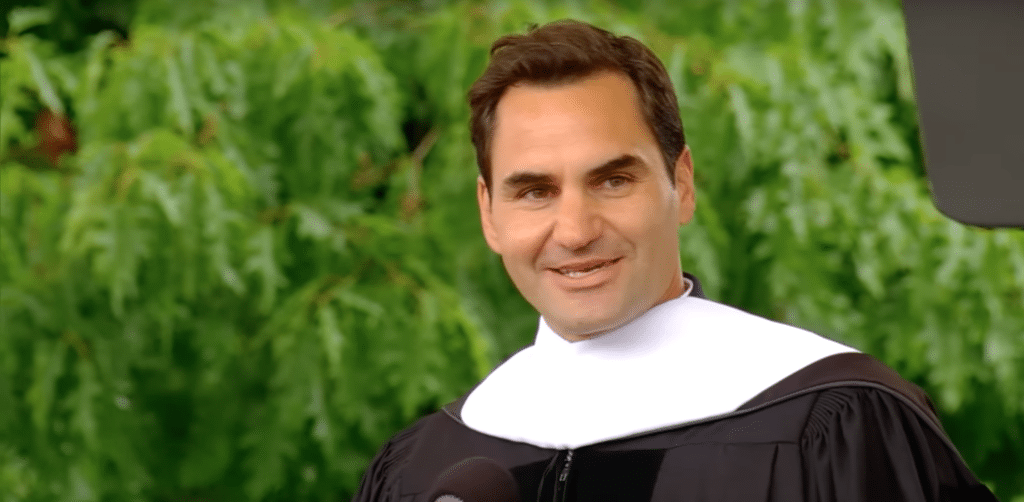 Roger Federer gives a commencement speech at Dartmouth. A man in a graduation gown, backgrounded by leaves.