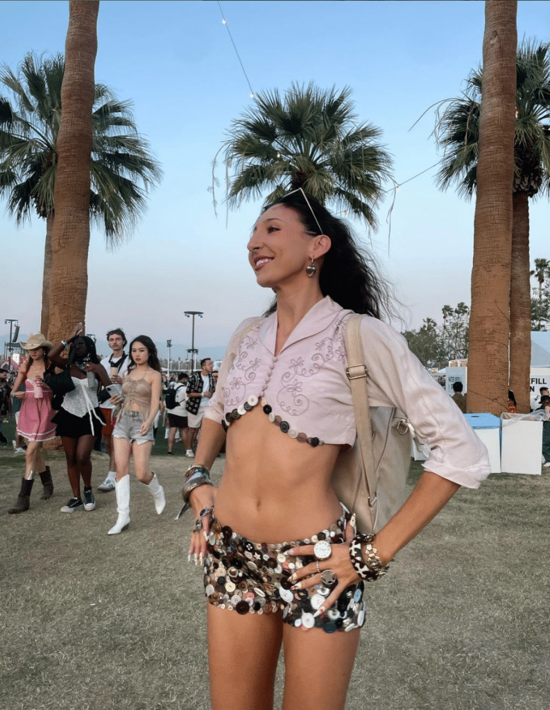 Woman standing in front of palm trees in a two piece button adorned outfit.