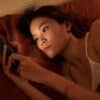 young woman scrolling on phone in bed